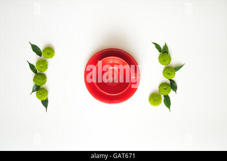 Red cup for coffee or tea with decoration of chrysanthemum flowers and ficus leaves on white background. Overhead view. Flat lay Stock Photo