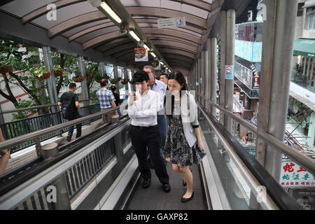 People on an escalator, some stand and use the smartphones others rush by and take over. Central to Mid-Levels escalator system Stock Photo