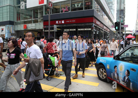 Lots of people crossing the street on a crossroad walking between cars that did not make the green light before turning to red. Kowloon, Hong Kong. Stock Photo