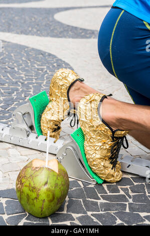 Brazilian athlete in gold running shoes crouching with a coconut at the start position in running blocks on Copacabana Beach Stock Photo