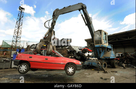 A giant mechanicial grabber lifts a car in the air, where metropolitan police officers check cars in a breakers yard in Harrow, North West London, after a rise in older cars being stolen and crushed for their scrap metal value and then being shipped overseas. Stock Photo