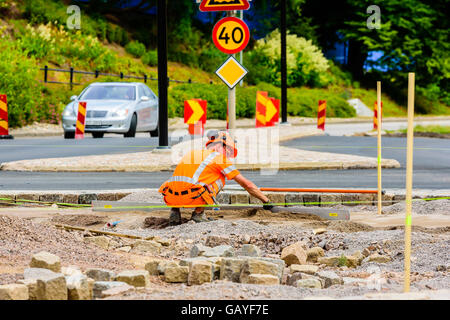 Motala, Sweden - June 21, 2016: Male worker squatting down and leveling the gravel building a roundabout. Car and traffic signs Stock Photo