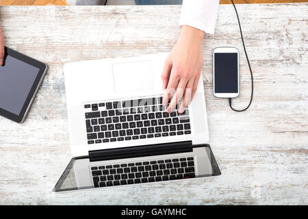 A young man using his laptop computer and various other devices on a desktop. Stock Photo
