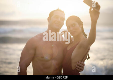 Young attractive man and woman are taking a selfie photo at the beach around sunset Stock Photo