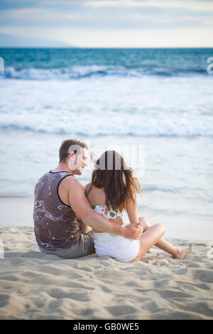 Back side of young couple in their 20s sitting at the beach Stock Photo