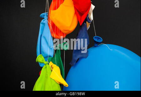 End of the party. Some burst, deflated balloons and one inflated balloon hanging on threads on black background. Stock Photo