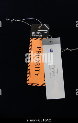 First class and premium travel. A British Airways First Class luggage label and Priority luggage label at Heathrow Airport. Stock Photo