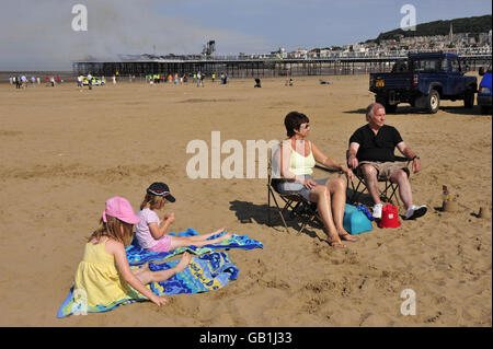 Weston-super-Mare pier fire. Tourists enjoy the sun on the beach by the Grand Pier at Weston-super-Mare after a major fire broke out. Stock Photo