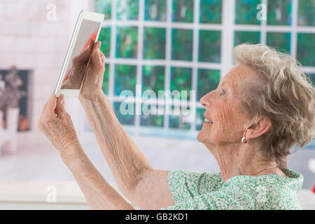 Happy mature grand mother taking photo of herself with tablet together at home Stock Photo