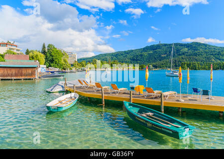 WORTHERSEE LAKE, AUSTRIA - JUN 20, 2015: tourist boats and sunchairs with umbrellas on wooden pier of beautiful alpine lake Wort Stock Photo