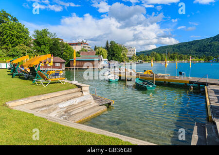 WORTHERSEE LAKE, AUSTRIA - JUN 20, 2015: tourist boats and sunchairs with umbrellas on wooden pier of beautiful alpine lake Wort Stock Photo