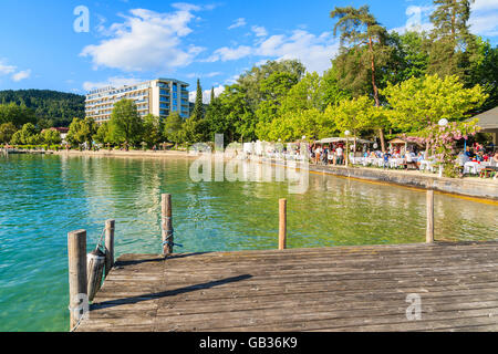 WORTHERSEE LAKE, AUSTRIA - JUN 20, 2015: wooden pier and people sitting at tables along Worthersee lake shore during summer beer Stock Photo