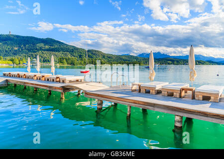 Sunchairs on wooden pier and view of beautiful alpine lake Worthersee in summer, Austria Stock Photo