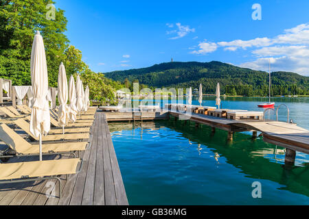 Sunchairs and beds on wooden deck and view of beautiful alpine lake Worthersee in summer time, Austria Stock Photo