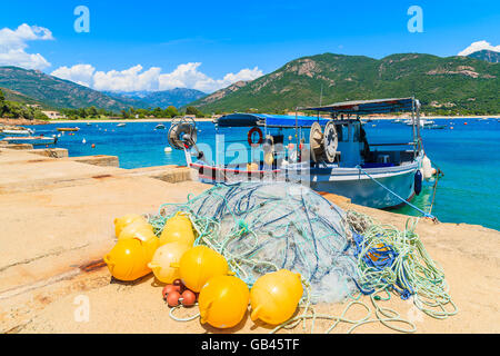 Fishing net in foreground with typical fishing boat in distance in small port on coast of southern Corsica island near Cargese t Stock Photo