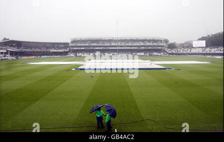 The covers are on as ground staff shelter under umbrellas when rain delays the start of the Fourth One Day International at Lord's Cricket Ground in London. Stock Photo