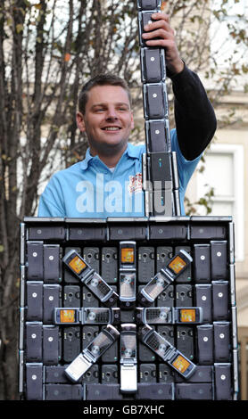 Photo. James Parker, of Moneysupermarket.com adds the final touch to a giant sculpture made entirely from old mobile phones which stands in Golden Square, central London. Stock Photo