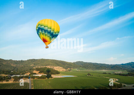 Bright yellow hot air balloon floats in blue sunny sky above Napa Valley, California Stock Photo