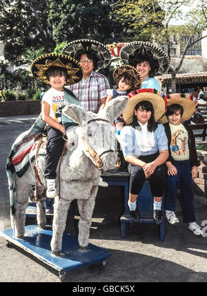 A family of six wearing sombrero hats poses for souvenir pictures with a toy donkey on Olvera Street in downtown Los Angeles, California, USA. This lively pedestrian street has been a Mexican marketplace since 1930 and attracts visitors with many vendor stands, shops and restaurants. It is part of El Pueblo de Los Angeles Historic Monument.