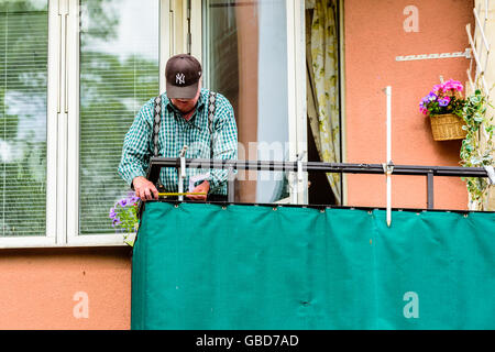 Motala, Sweden -June 21, 2016: Senior man measuring at a balcony. Ha has a small piece of paper in his hand as well. Stock Photo