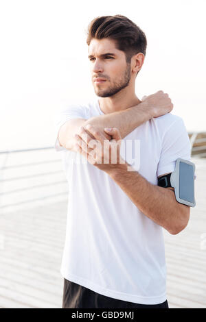 Handsome young man athlete with mobile phone in armband stretching arms Stock Photo
