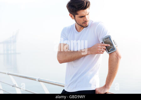 Pensive young sportsman using blank screen mobile phone on armband Stock Photo