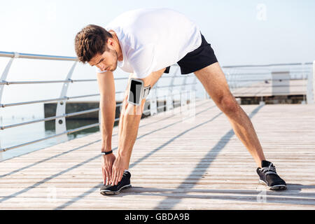 Handsome young sportsman stretching legs during workout on pier Stock Photo