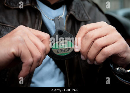 Taxi driver Tony Bernard holds up his taxi drivers badge as he protests against a new scheme for minicabs in Westminster, central London. Stock Photo