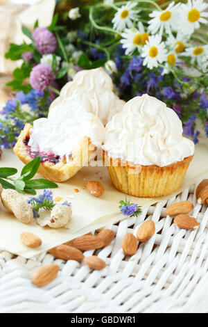 Cupcakes with blueberries and white cream. Bright wild flowers on the background Stock Photo
