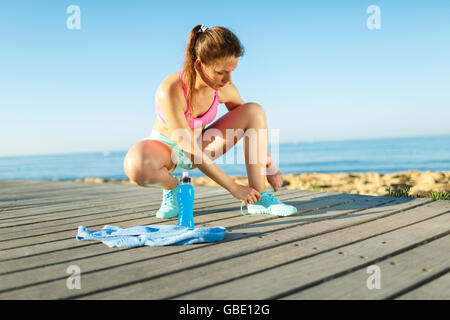 Running shoes - woman tying shoe laces. Closeup of female sport fitness runner getting ready for jogging outdoors on waterfront Stock Photo