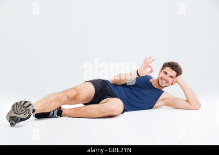 Relaxed young athletic man lying and showing ok sign over white background Stock Photo