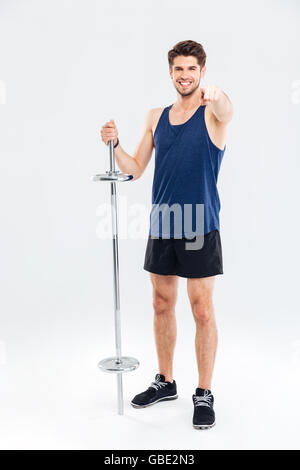 Young handsome sportsman holding barbell and pointing finger at camera isolated on a gray background Stock Photo