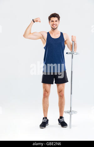 Young handsome smiling sportsman holding barbell and showing biceps isolated on a gray background Stock Photo