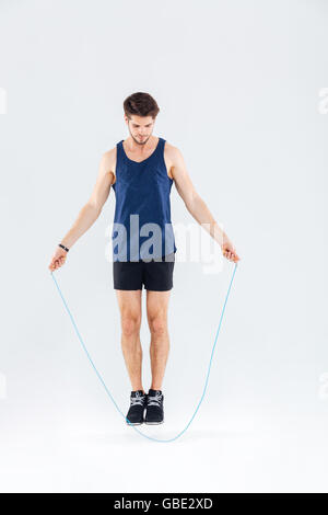 Full length portrait of a man jumping with skipping rope isolated on a gray background Stock Photo