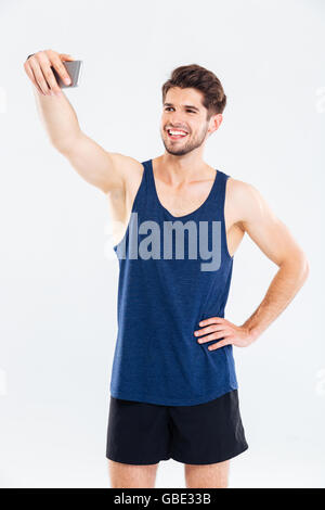 Smiling young sportsman standing and talking selfie with cell phone over white background Stock Photo