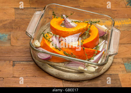 Sliced pumpkin with red onion, garlic and thyme in a baking dish Stock Photo