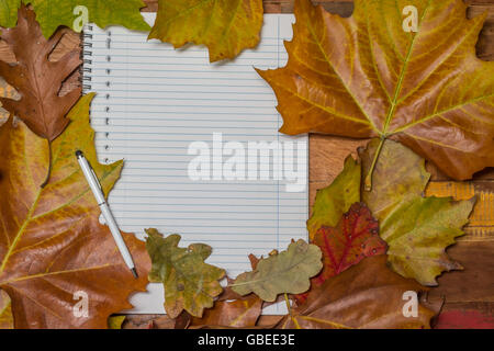 Notepad and pen with autumn leaves on a wooden table Stock Photo