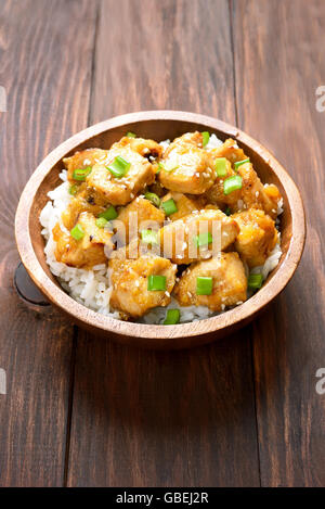 Chicken meat with orange sauce and rice in wooden bowl Stock Photo