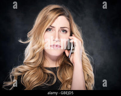 Woman calling with a cell phone over dark background. Stock Photo