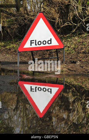 General view of a Flood warning sign situated next to a large flood on a small B-road Stock Photo