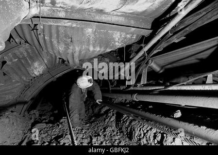 A pit official at Sutton Colliery near Mansfield, Nottinghamshire, checks on a trunk conveyor at the coal face. Stock Photo