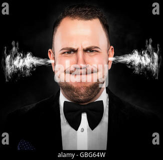 Stressful man with smoke or fume coming out from his ears on dark background. Stock Photo