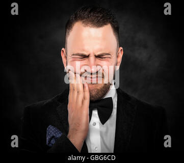 A young man feels toothache over dark background. Stock Photo