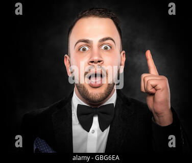 Idea. Young man shows finger up over darck background. Stock Photo