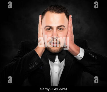 Man in suit covering his ears over dark background. Stock Photo