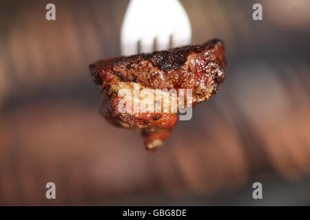 Piece of Rare Beef Meat on a Plastic Fork. Piece of sinta steak on a disposable fork, close up. Red meat stuck on a white plastic fork. Bon Appetit! Stock Photo