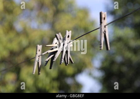 Wooden Clothespins Hanged on a Clothesline. Group of old wooden laundry sticks hanged on an iron clothe line after long time with no use. Clothesline Stock Photo