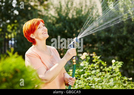 Senior woman watering her plants in his garden with sprinkle Stock Photo