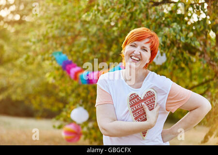Happy senior woman with a heart on her hand in summer at a park Stock Photo