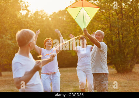 Happy senior citizens group playing flying a kite in the park in autumn Stock Photo